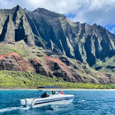 A boat on blue water with rugged cliffs and green vegetation in the background under a partly cloudy sky.