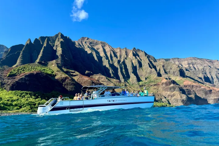 Boat with people near mountainous coastline under clear blue sky