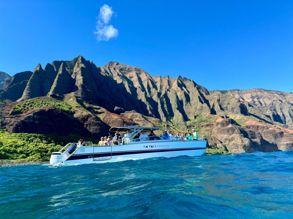Boat with people near mountainous coastline under clear blue sky