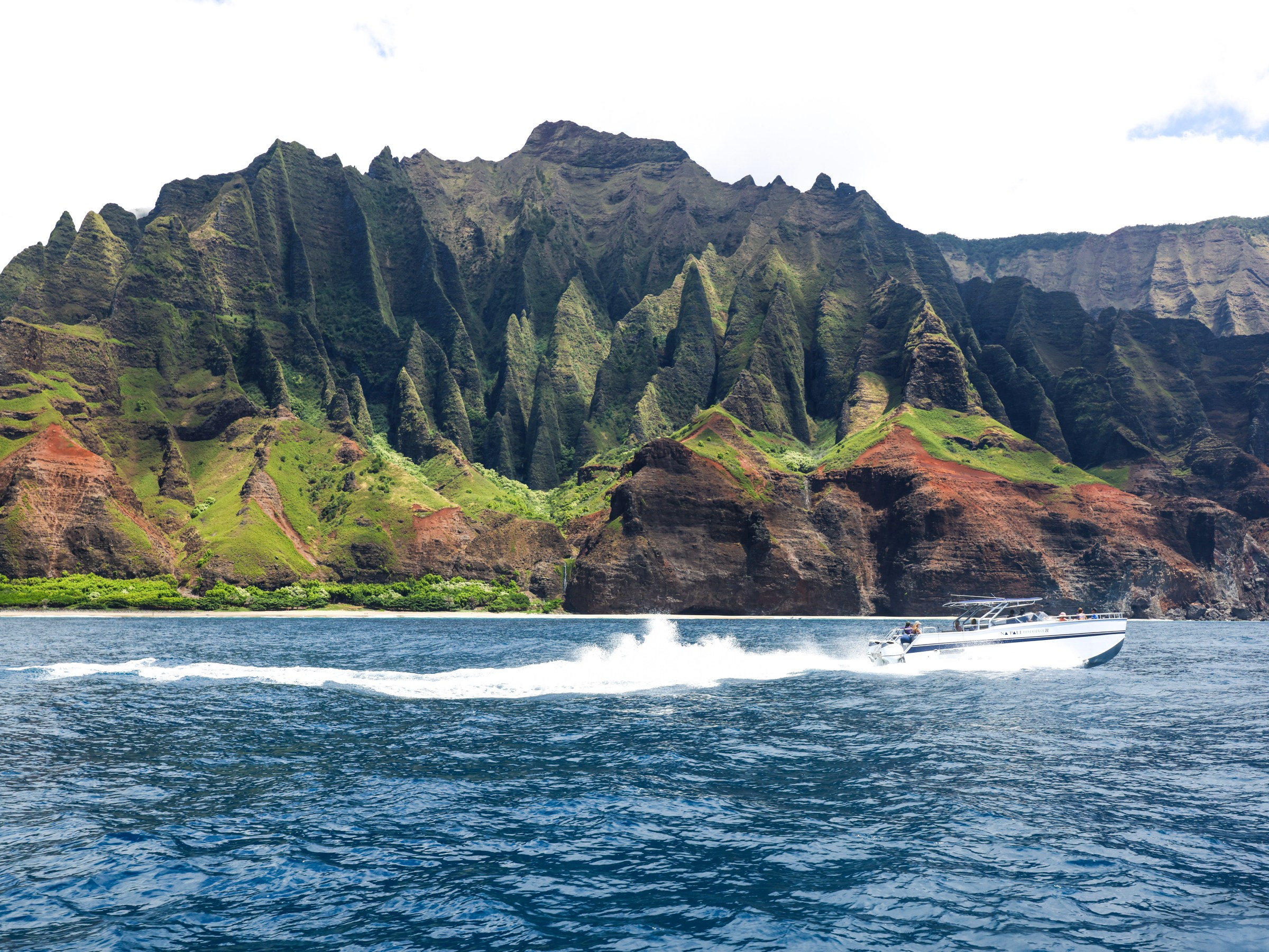 Speedboat on ocean with green cliffs in the background.