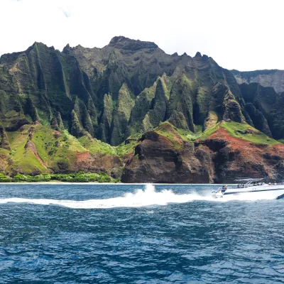 Speedboat on ocean with green cliffs in the background.