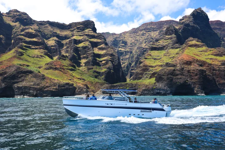 Boat sailing near rugged coastal cliffs under a blue sky.