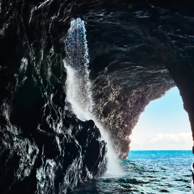 Water cascading inside a rocky cave with ocean visible through the opening.