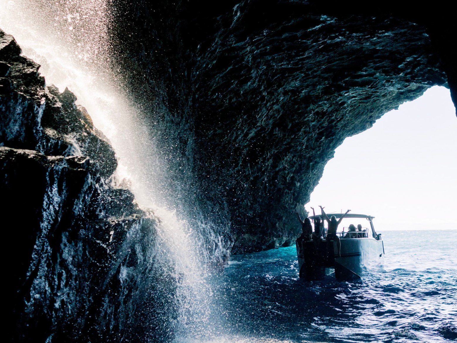 A boat inside a sea cave with rock formations and a waterfall cascading from above.