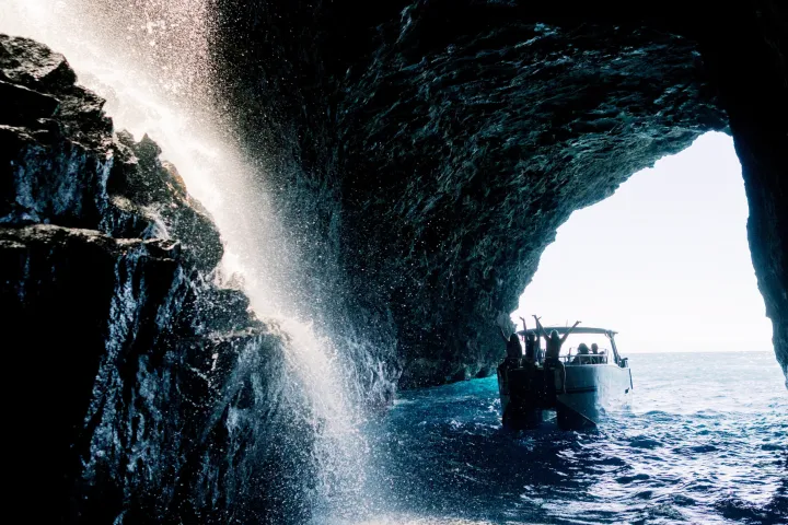 A boat inside a sea cave with rock formations and a waterfall cascading from above.