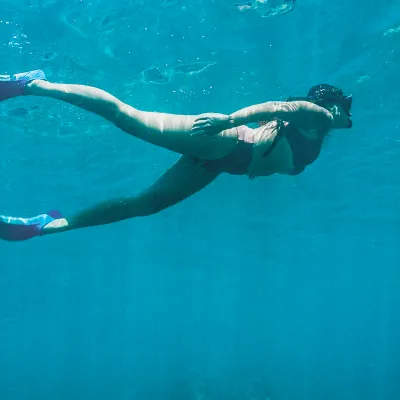Person snorkeling underwater with pink fins, wearing swimwear.