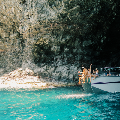 People jumping off a boat into turquoise water inside a rocky cave.
