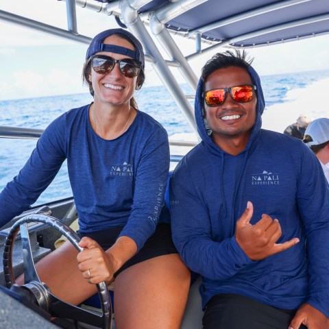 Two smiling people in blue shirts on a boat with ocean in the background.