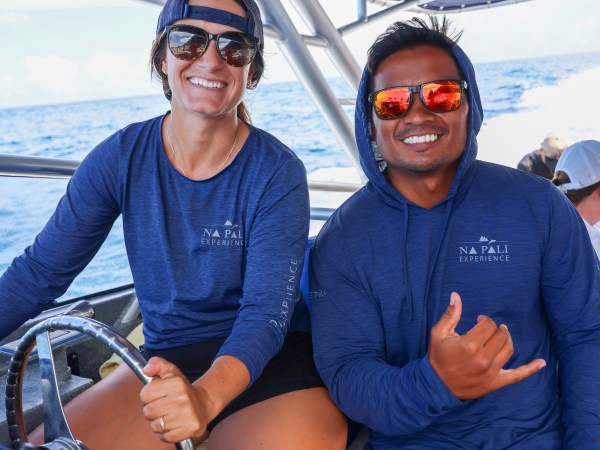 Two smiling people in blue shirts on a boat with ocean in the background.