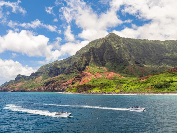 Coastal view of lush green mountains with two boats on a blue ocean under a partly cloudy sky.