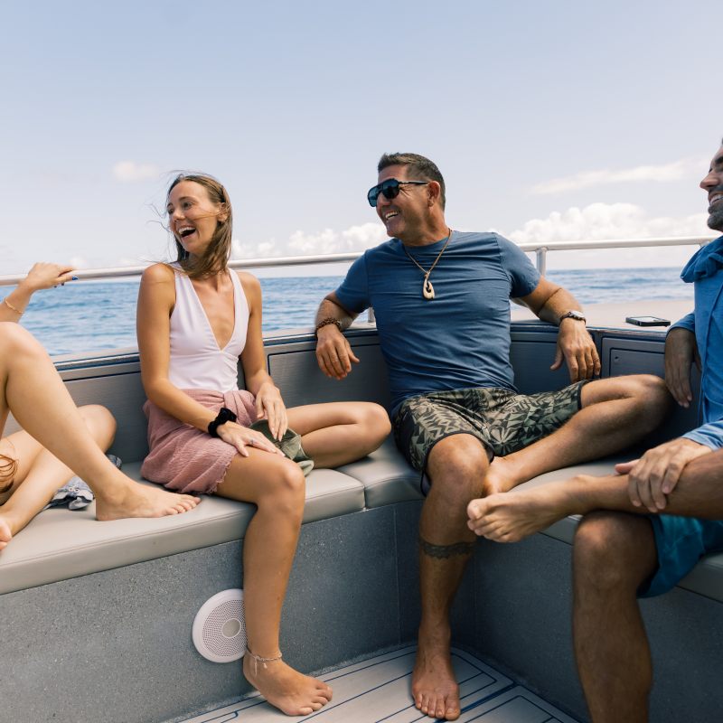 Four people smiling and talking on a boat with an ocean view.