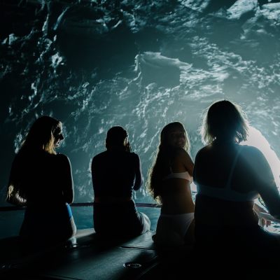 Four people silhouetted on a boat inside a cave with a bright entrance.