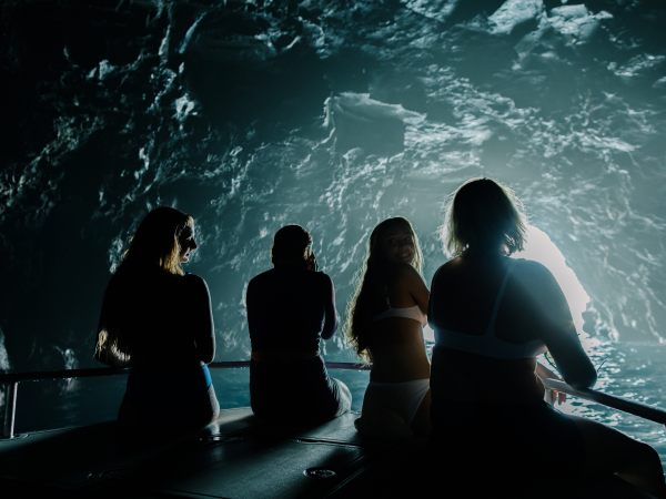 Four people silhouetted on a boat inside a cave with a bright entrance.