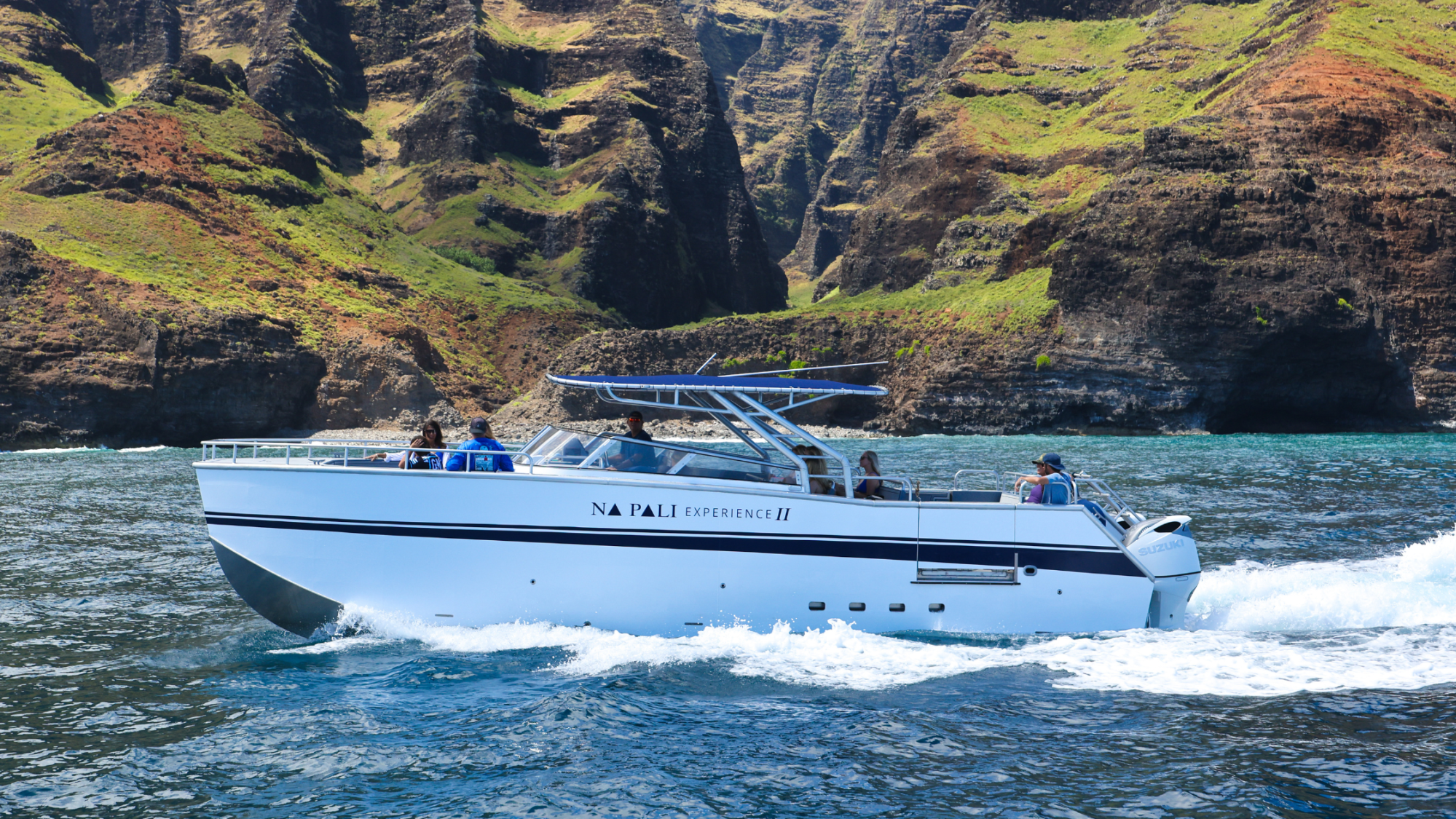 Boat with passengers cruising by rocky cliffs and clear blue water.