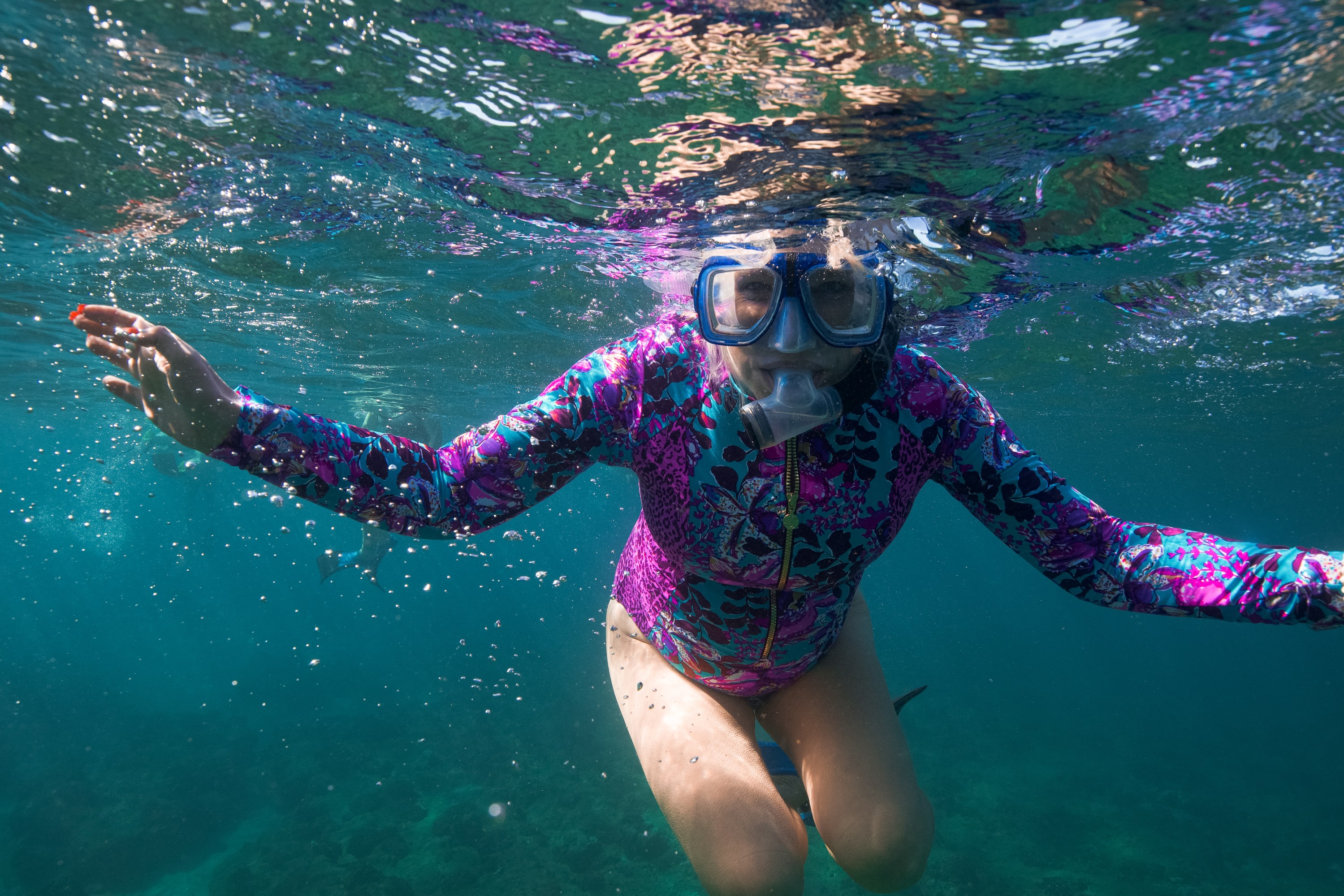 Person snorkeling in clear water wearing a patterned wetsuit and mask.