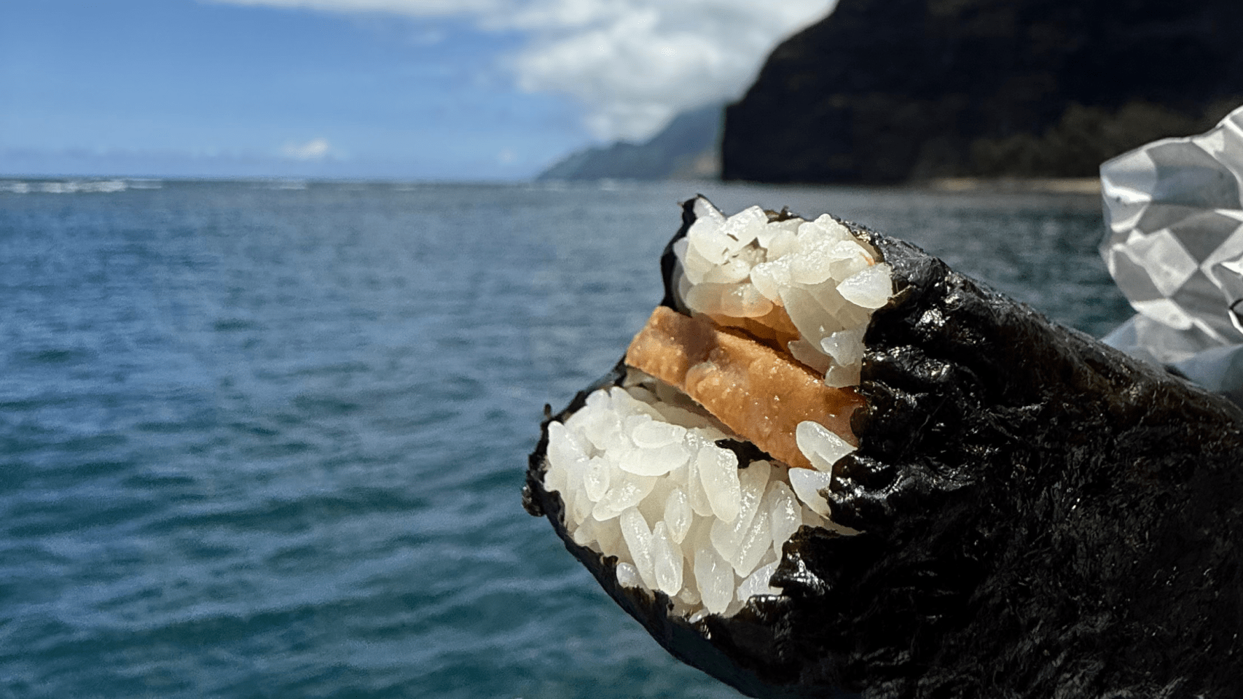 Musubi with ocean and cliffs in the background.